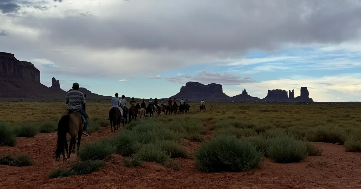 A line of riders on horseback crossing the desert toward the buttes of Monument Valley