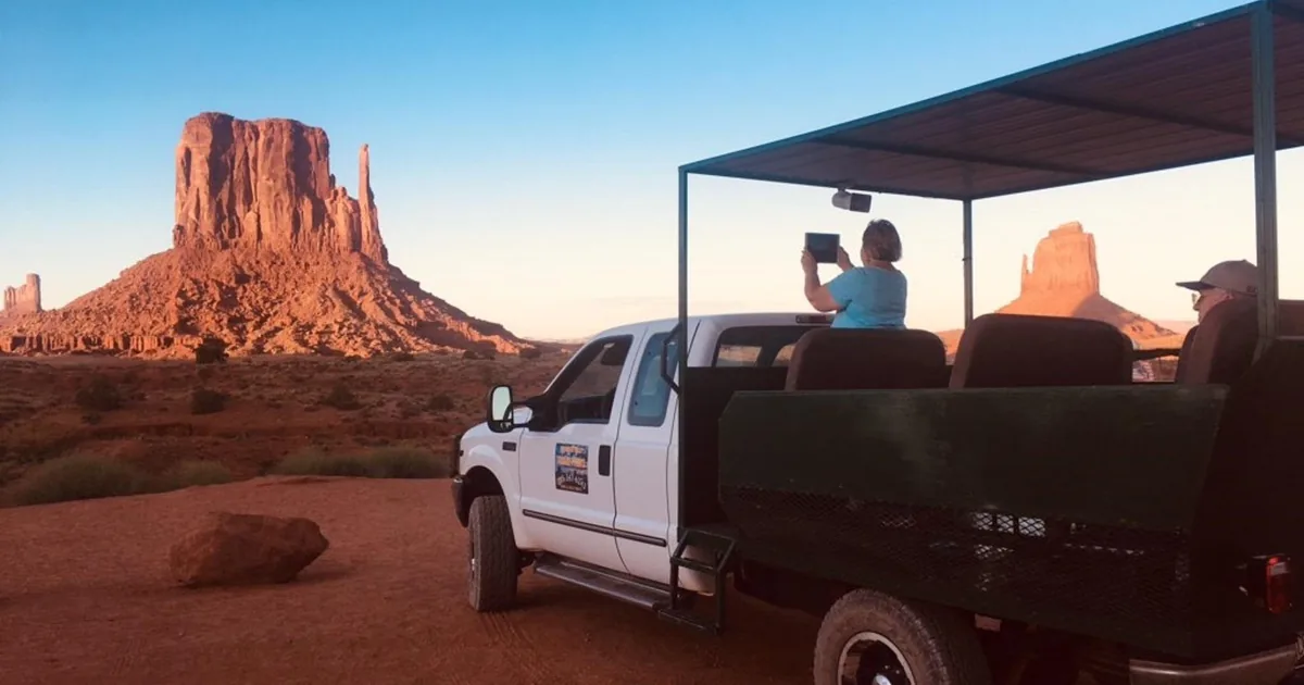 An open-air tour truck on the sand road below the buttes of Monument Valley