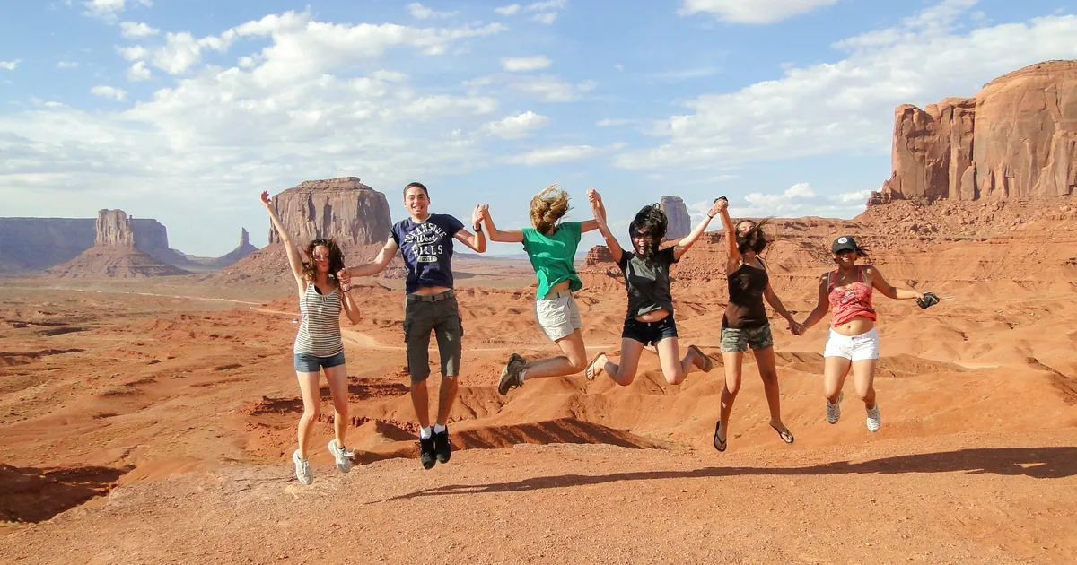 A small tour group jumping for a photo on the red sand of Monument Valley